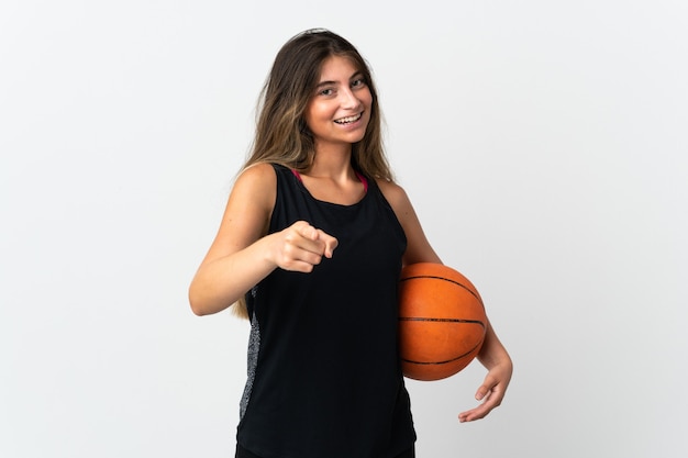 Junge kaukasische Frau lokalisiert auf weißer Wand, die Basketball spielt und nach vorne zeigt