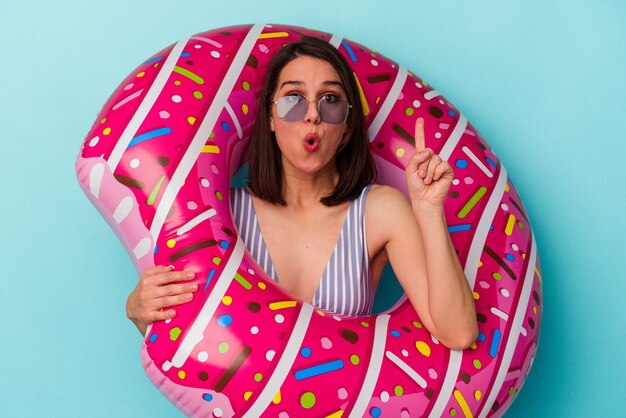 Junge kaukasische Frau mit aufblasbarem Donut isoliert auf blauem Hintergrund mit einer großartigen Idee, Konzept der Kreativität.