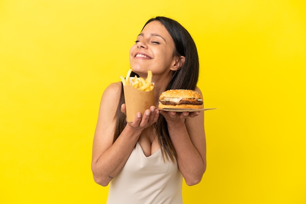 Junge kaukasische Frau mit Burger und Pommes auf gelbem Hintergrund isoliert