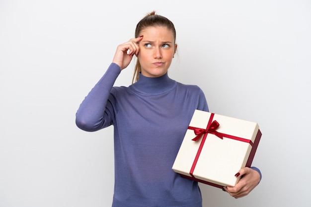 Foto junge kaukasische frau mit einem geschenk isoliert auf weißem hintergrund mit zweifeln und verwirrtem gesichtsausdruck