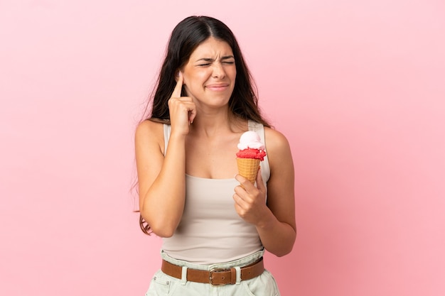 Junge kaukasische Frau mit einem Kornett-Eis isoliert auf rosa Hintergrund frustriert und bedeckt die Ohren