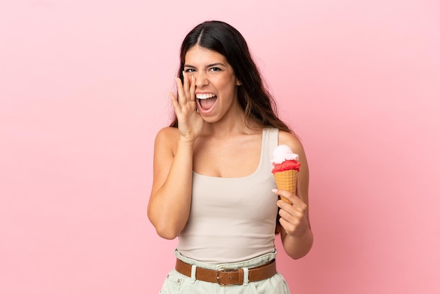 Junge kaukasische Frau mit einem Kornett-Eis isoliert auf rosa Hintergrund schreien mit weit geöffnetem Mund