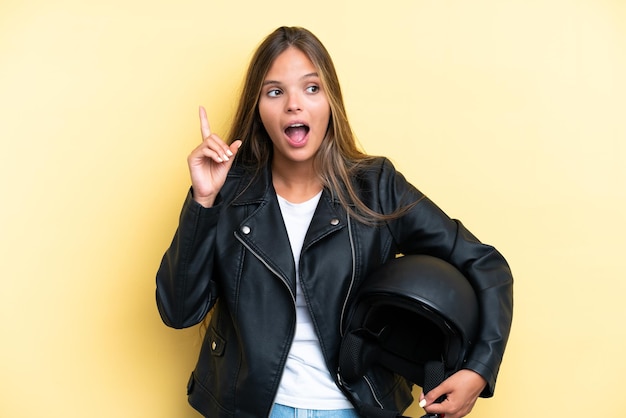 Junge kaukasische Frau mit einem Motorradhelm auf gelbem Hintergrund isoliert, die eine Idee denkt und mit dem Finger nach oben zeigt