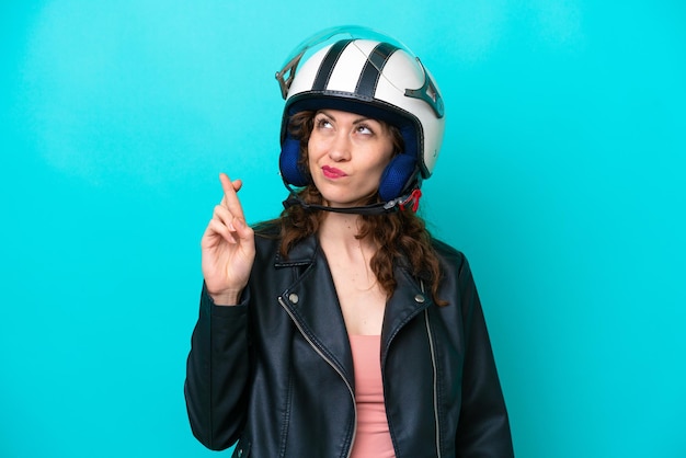 Junge kaukasische Frau mit einem Motorradhelm, der auf blauem Hintergrund isoliert ist, die Daumen drückt und das Beste wünscht