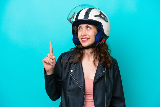 Junge kaukasische Frau mit einem Motorradhelm, der auf blauem Hintergrund isoliert ist und eine großartige Idee zeigt