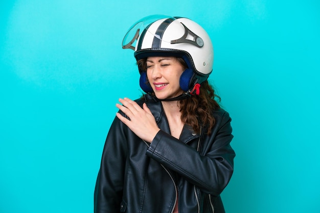 Junge kaukasische Frau mit einem Motorradhelm isoliert auf blauem Hintergrund, die unter Schmerzen in der Schulter leidet, weil sie sich Mühe gegeben hat