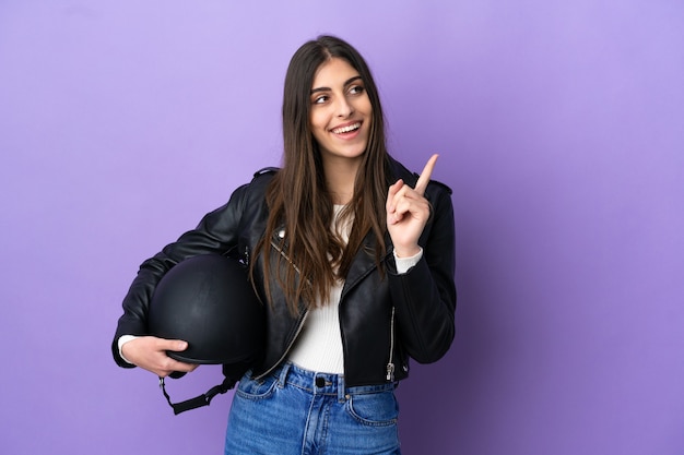 Junge kaukasische Frau mit einem Motorradhelm isoliert auf lila Hintergrund, der auf eine großartige Idee zeigt