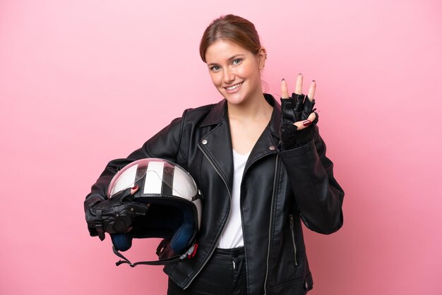 Junge kaukasische Frau mit einem Motorradhelm isoliert auf rosa Hintergrund glücklich und zählt drei mit den Fingern