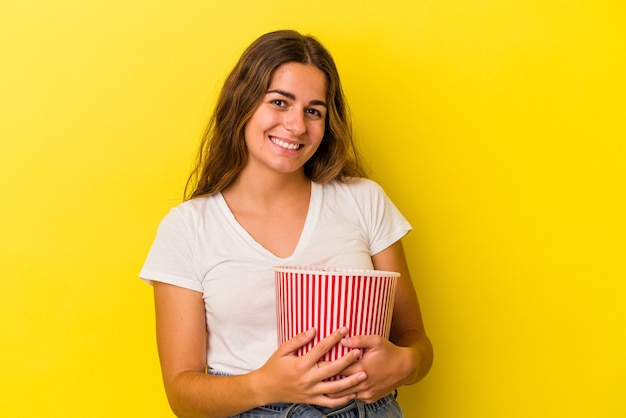Junge kaukasische Frau mit einem Popcorn isoliert auf gelbem Hintergrund glücklich, lächelnd und fröhlich.