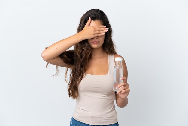 Junge kaukasische Frau mit einer Flasche Wasser lokalisiert auf weißem Hintergrund, der die Augen mit den Händen bedeckt. Will was nicht sehen