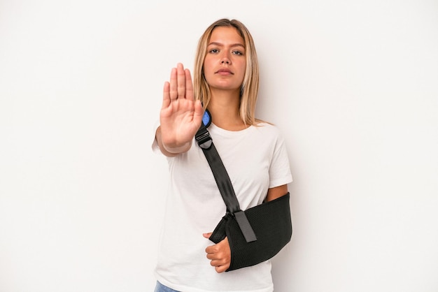 Junge kaukasische Frau mit gebrochener Hand isoliert auf weißem Hintergrund, die mit ausgestreckter Hand steht und Stoppschild zeigt und Sie verhindert.