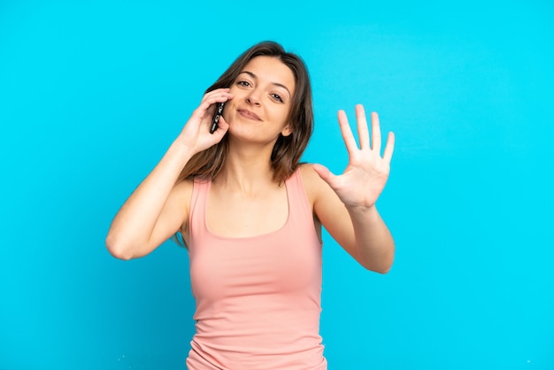 Junge kaukasische Frau mit Handy isoliert auf blauem Hintergrund und zählt fünf mit den Fingern