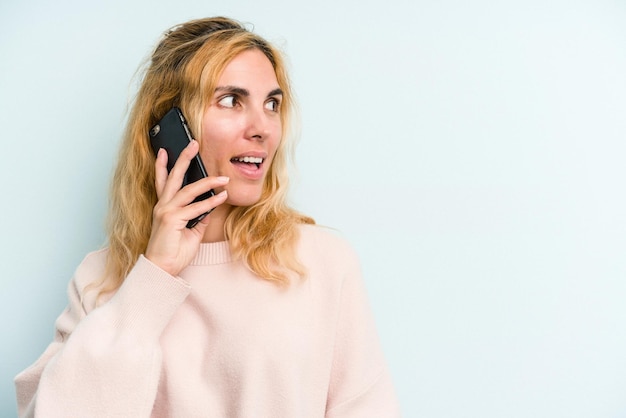 Junge kaukasische Frau mit Handy isoliert auf blauem Hintergrund