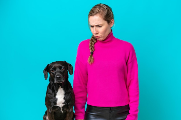Junge kaukasische Frau mit ihrem Hund isoliert auf blauem Hintergrund mit traurigem Ausdruck