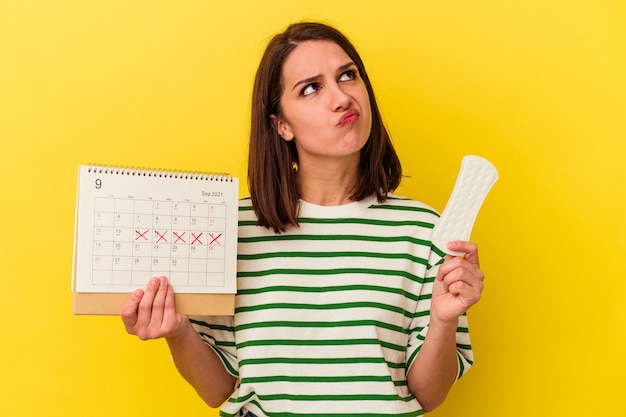 Junge kaukasische Frau mit Kalender und Kompresse isoliert auf gelbem Hintergrund