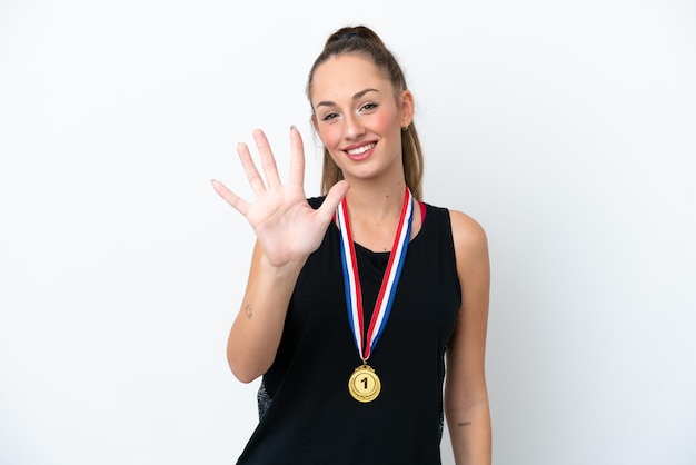 Junge kaukasische Frau mit Medaillen lokalisiert auf weißem Hintergrund, die fünf mit den Fingern zählt