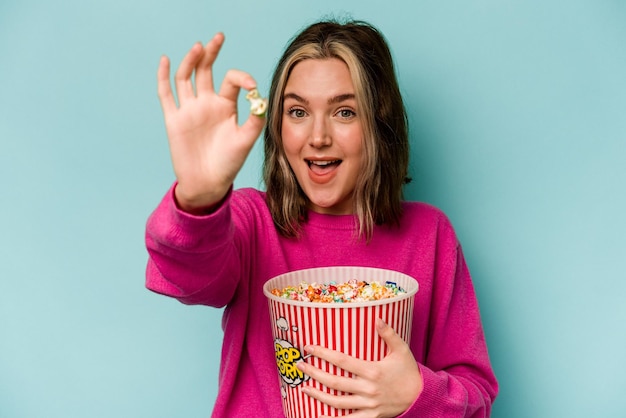 Junge kaukasische Frau mit Popcorn isoliert auf blauem Hintergrund