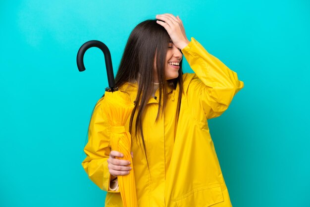 Junge kaukasische Frau mit regenfestem Mantel und Regenschirm isoliert auf blauem Hintergrund hat etwas erkannt und beabsichtigt die Lösung
