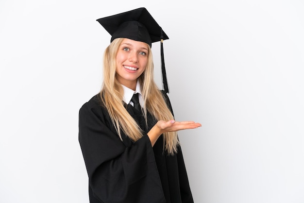 Junge kaukasische Frau mit Universitätsabschluss isoliert auf weißem Hintergrund, die eine Idee präsentiert, während sie lächelnd in Richtung schaut