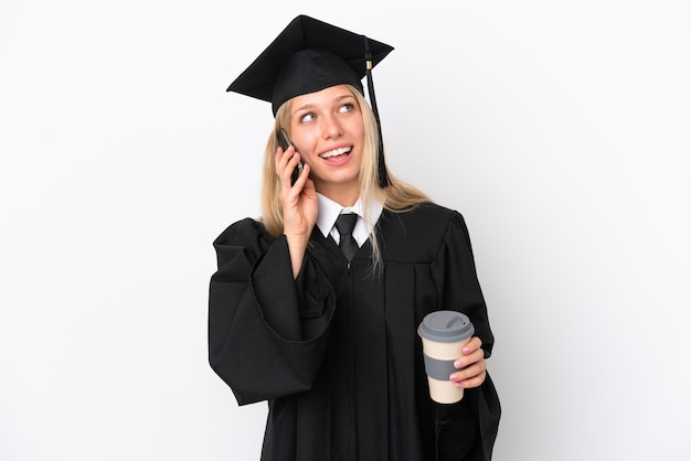 Junge kaukasische Frau mit Universitätsabschluss isoliert auf weißem Hintergrund mit Kaffee zum Mitnehmen und einem Handy