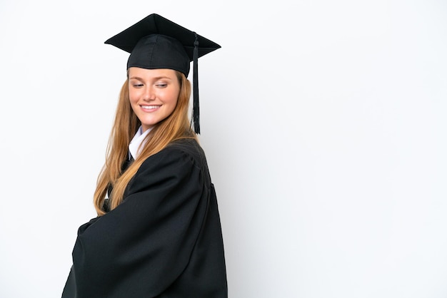 Junge kaukasische Frau mit Universitätsabsolvent isoliert auf weißem Hintergrund mit verschränkten Armen und glücklich