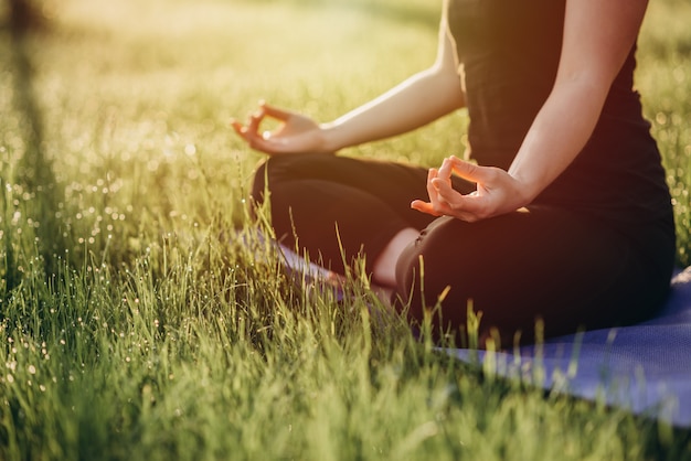 Junge kaukasische Frau praktiziert Yoga in Lotussitz an einem frühen sonnigen Morgen in einem Wald mit Gras und Tau Weicher selektiver Fokus.