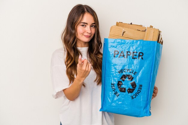 Junge kaukasische Frau Recycling-Papier isoliert auf weißem Hintergrund zeigt mit dem Finger auf Sie, als ob Sie einladen, näher zu kommen.