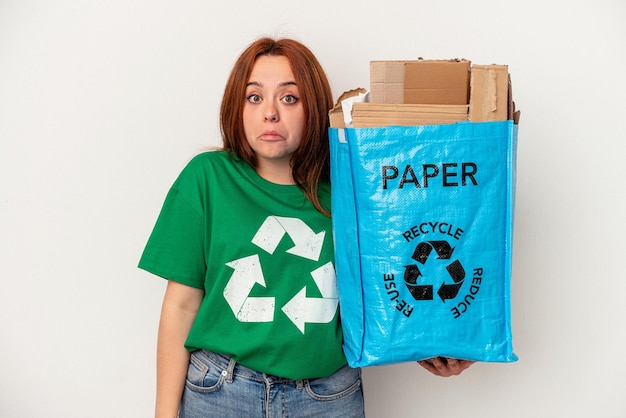 Junge kaukasische Frau Recyclingpapier isoliert auf weißem Hintergrund zuckt mit den Schultern und offene Augen verwirrt.