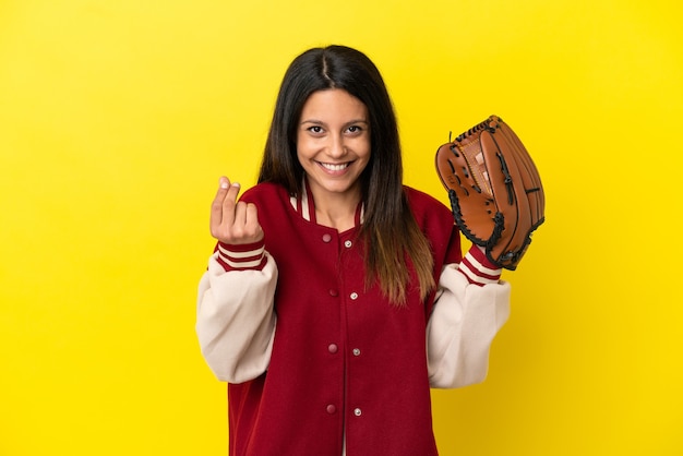 Junge kaukasische Frau spielt Baseball isoliert auf gelbem Hintergrund und macht Geldgeste