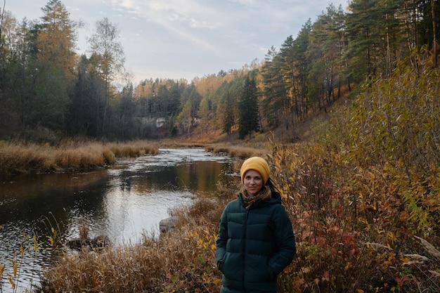 Junge kaukasische Frau steht im Herbst in der Nähe des Flusses und lächelt