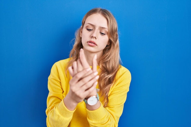 Junge kaukasische Frau steht vor blauem Hintergrund und leidet unter Schmerzen an Händen und Fingern, Arthritis-Entzündung
