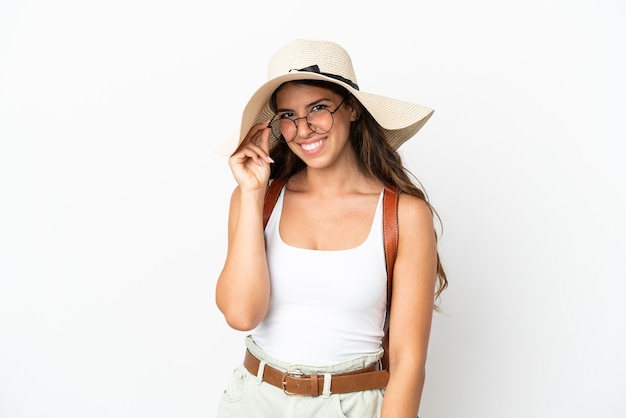 Junge kaukasische Frau trägt eine Pamela in den Sommerferien isoliert auf weißem Hintergrund mit Brille und glücklich