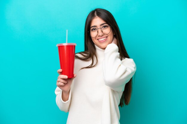 Junge kaukasische Frau trinkt Soda isoliert auf blauem Hintergrund lachend