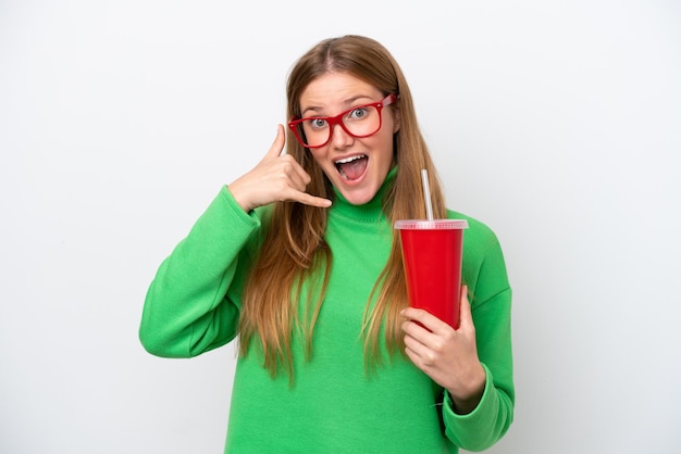 Junge kaukasische Frau trinkt Soda isoliert auf weißem Hintergrund und macht eine Telefongeste. Rufen Sie mich zurück