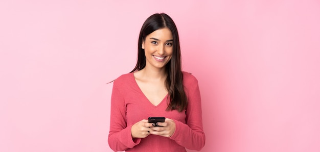 Junge kaukasische Frau über isolierter Wand, die eine Nachricht mit dem Handy sendet