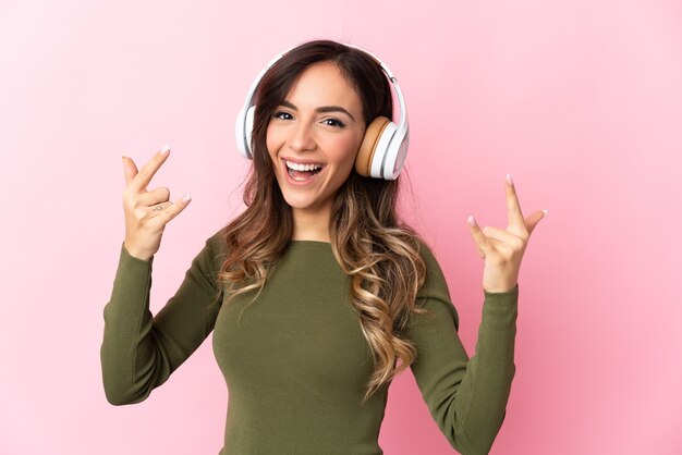 Junge kaukasische Frau über isolierter Wand, die Musik hört, die Rockgeste macht