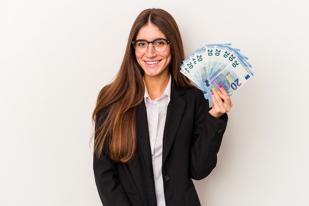 Junge kaukasische Geschäftsfrau, die Banknoten lokalisiert auf weißem Hintergrund hält glücklich, lächelnd und fröhlich.