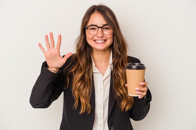 Junge kaukasische Geschäftsfrau, die einen Kaffee zum Mitnehmen isoliert auf weißem Hintergrund hält und fröhlich lächelt und die Nummer fünf mit den Fingern zeigt.