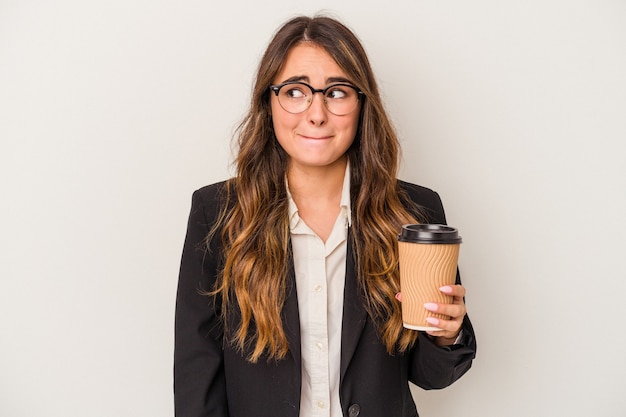 Junge kaukasische Geschäftsfrau, die einen Kaffee zum Mitnehmen lokalisiert auf weißem Hintergrund verwirrt hält, fühlt sich zweifelhaft und unsicher.