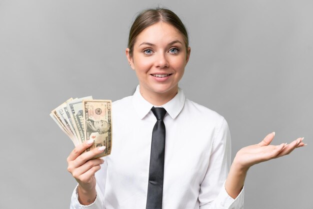 Junge kaukasische Geschäftsfrau, die Geld über isoliertem Hintergrund mit schockiertem Gesichtsausdruck hält