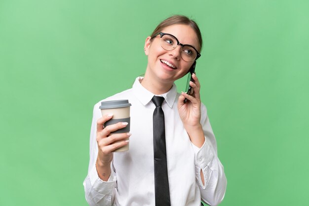 Junge kaukasische Geschäftsfrau mit isoliertem Hintergrund, die Kaffee zum Mitnehmen und ein Handy hält