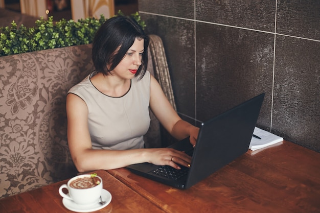 Junge kaukasische Geschäftsfrau mit Laptop und Notizbuch. Frau im Café