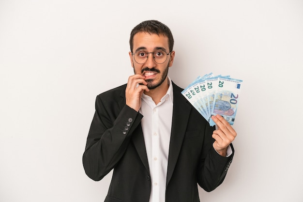 Junge kaukasische Geschäftsmann hält Banknoten isoliert auf weißem Hintergrund beißende Fingernägel, nervös und sehr ängstlich.