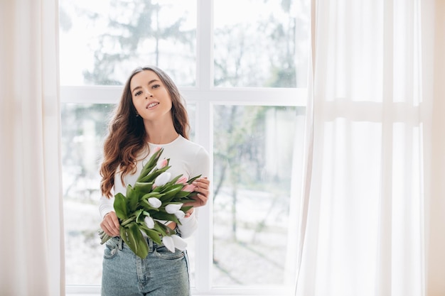 Junge kaukasische glückliche Frau, die zu Hause einen Strauß frischer Tulpen riecht.