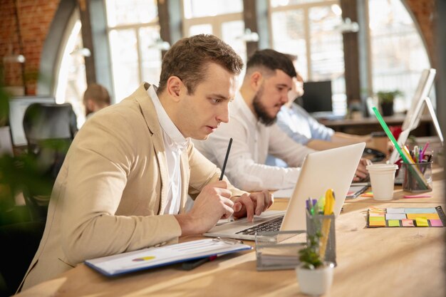 Junge kaukasische Kollegen, die in einem Büro mit modernen Geräten und Gadgets zusammenarbeiten