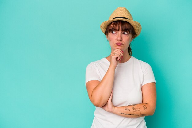 Junge kaukasische kurvige Frau isoliert auf blauem Hintergrund, die seitlich mit zweifelhaftem und skeptischem Ausdruck schaut.