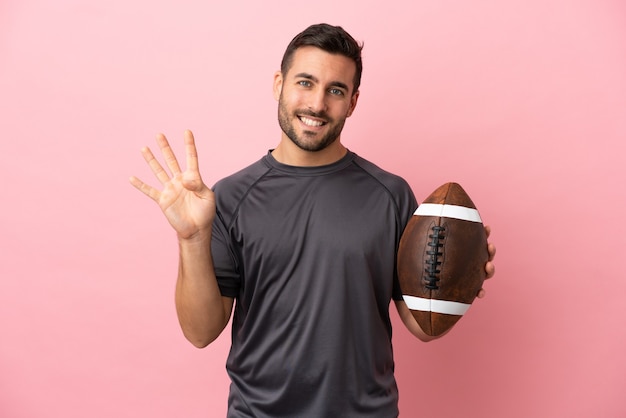 Junge kaukasische Mann spielt Rugby isoliert auf rosa Hintergrund glücklich und zählt vier mit den Fingern