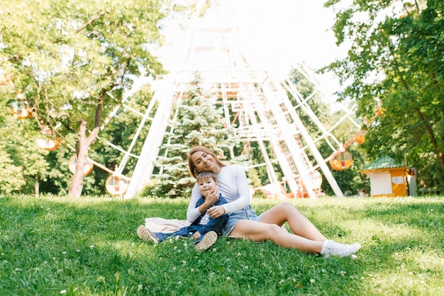 Junge kaukasische Mutter und ihr kleiner Sohn sitzen im Sommer im Gras im Park und entspannen sich im Freien