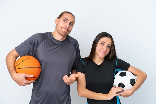 Junge kaukasische Paare, die Basketball und Fußball spielen, isoliert auf weißem Hintergrund, machen Zweifel, während sie die Schultern heben