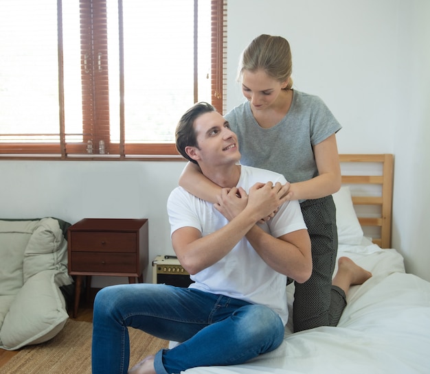 Junge kaukasische Paarfrau umarmt Mann zurück auf Bett mit Liebe auf Bett im Schlafzimmer zu Hause.